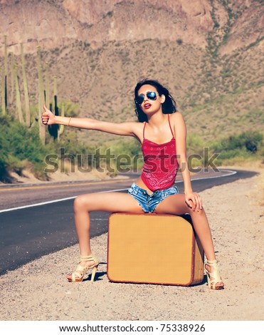 Beautiful young lady with case hitching a ride on a lonely hot desert road