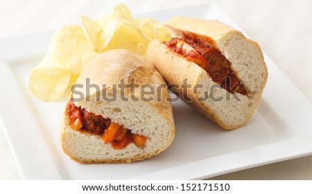 Sausage and Peppers Sandwich - Sausage and peppers sandwich served with a side of potato chips.