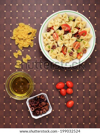 A bowl of pasta salad and the ingredients to make it.