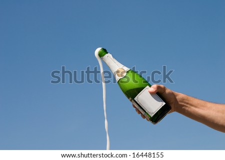 Hand holding an open bottle of champagne on a background of the blue sky