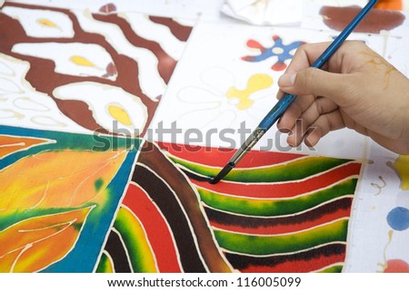 An artist carefully paint the pattern on a white traditional batik fabric