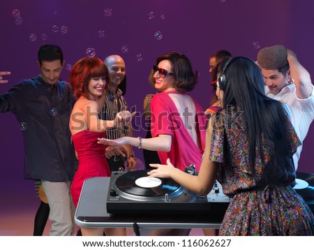 two young girls dancing and enjoying the party, with othe people dancing in the background and with dj mixing music