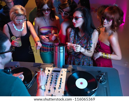 young women holding drinks and talking to the dj at a party