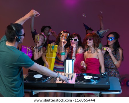 young women dancing at party and playing with party horns, with dj mixing and dancing and people dancing in the background