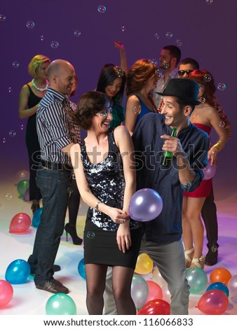 couple laughing and dancing, in front of ogroup of men and women at party, with balloons and bubbles