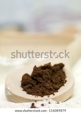 closeup detail of some brown, powder condiment, placed on a wooden spoon , on a bed of flour