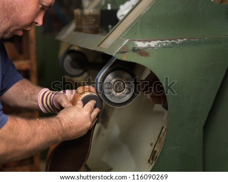 adult man working in a shoe factory, finishing the soles of the shoes, at a machine