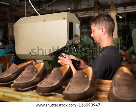 adult man working in a shoe factory, sewing the soles of the shoes, at a machine