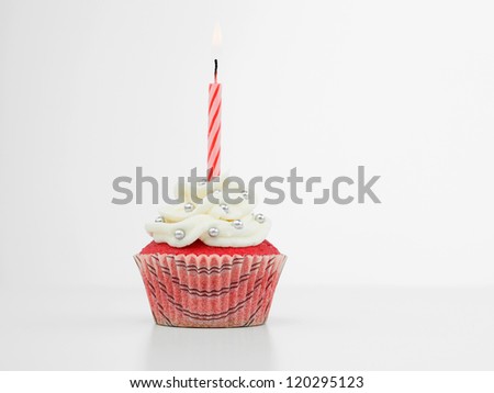 red muffin with cream  white and candy silve one red spiral burning candle on white background isolated