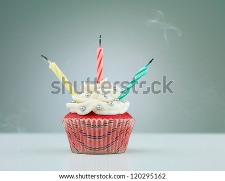 muffin on the table with three lit candles on neutral background with gradient