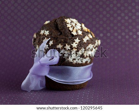 single chocolate muffin, decorated with white sugar stars, wrapped up with a ribbon, on a purple polka dots paper