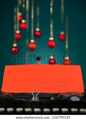 closeup of a typewriter with the beginning of a letter to santa written on red paper with red blurred christmas globes on blue background