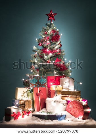 green christmas tree with beatiful red decorations surrounded by a heap of gift boxes covered with snow o blue gradient background