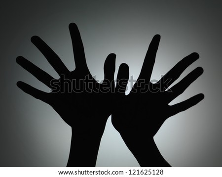 two hands silhouette with fingers spread backlit on grey gradient background
