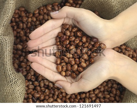 beans in heart shape held in hands over a raffia bag