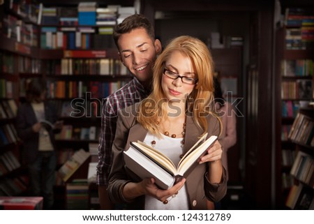 close-up of attractive young couple in a library reading a book together with other people and bookshelves in background