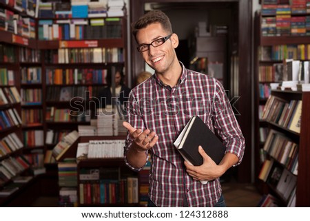 close-up of young caucasian handsome guy with eyeglasses and book in his hands, in a bookstore