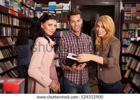 close-up of three young good looking people in a bookstore turning the pages of a book, smiling