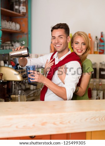 young caucasian couple hugging and pouring a drink from a shaker into a colorful glass behind a counter