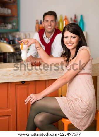 young beautiful caucasian girl sitting at a bar drinking a cocktail an smoking a cigarette with a guy behind the counter