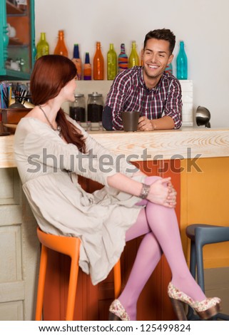 two young caucasian people sitting at the counter in a colorful cafe socializing and having fun