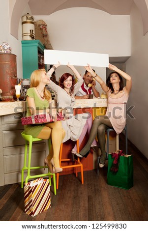 young attractive caucasian people in colorful cafe holding an empty ad banner with shopping bags around them
