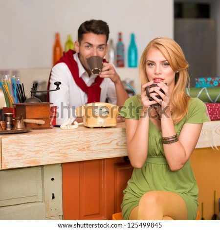 close-up of beautiful blonde girl drinking a coffee and a handsome guy behind the counter in a cafe