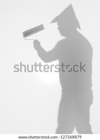 side view of man with paint roller in his hand and a hat  in shape of tringle on his head, behind a diffuse surface