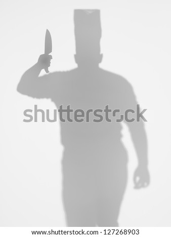 front view of man with a cooker\'s hat holding a kitchen knife in his hand, behind a diffuse surface