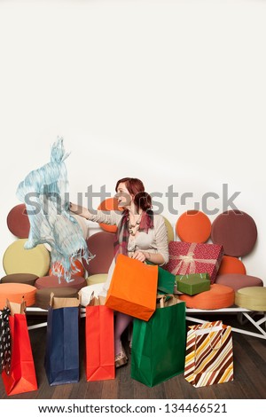 young woman pulling out a scarf from a shopping bag, sitting on a sofa