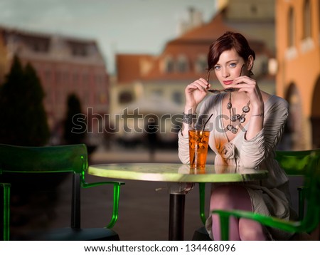 young woman sitting at a table in a city square and having a drink
