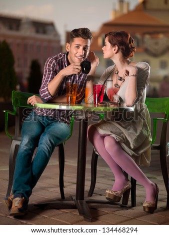 young man and woman whispering something at a man\'s year, on a terrace