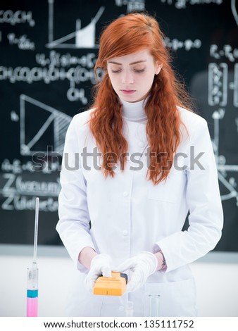 close-up of a girl student in a chemistry lab scanning objects and lab tools with a blackboard on the background