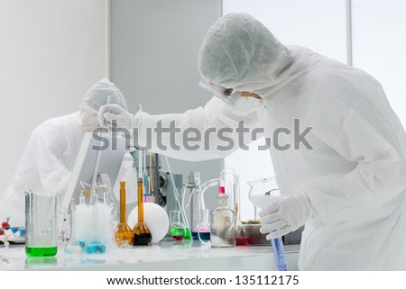 close-up of a man studying a chemical reaction on a lab table with lab tools  colorful liquids and another one in the background chemically analysing substances