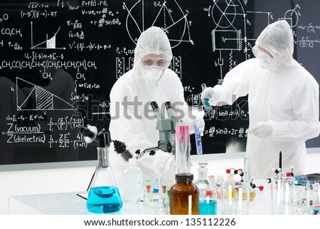 general-view of two people studying and testing substances in a lab with lab tools and colorful liquids and a blackboard with chemical formulas on the background
