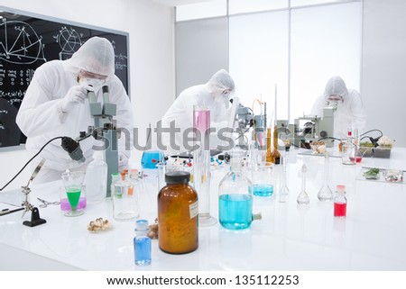 general-view of  three people observing and analysig chemical reactions in a lab  using colorful substances and lab tools  on a lab worktable with a blackboard on the background