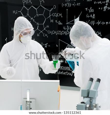 close-up of two people chemically testing substances in a laboratory with transparent tools and colorful liquids with a blackboard on the background