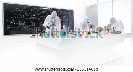 general-view of three people analysing  substances in a chemistry lab using colorful liquids and lab tools with a blackboard with chemical formulas on the background