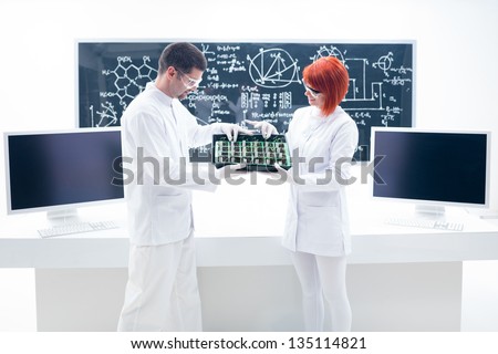 general view of two people analyzing seedlings on a chemistry lab with a worktable and a blackboard on the background