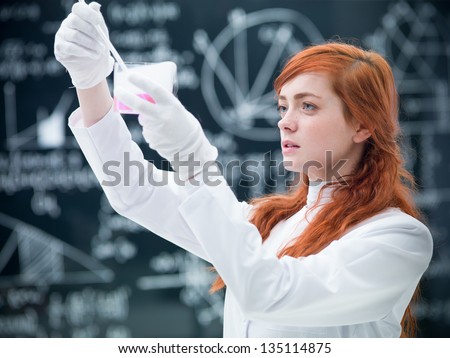 close-up of student in a chemistry lab analysing and observing colorful  liquids reactions and magical gas with a blackboard on the background
