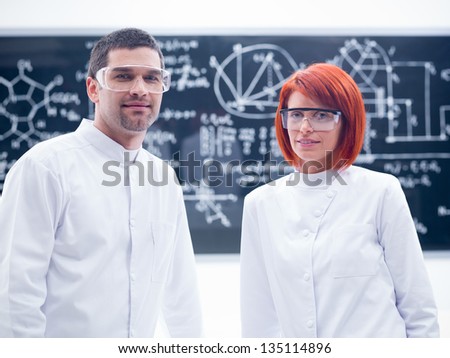 close-up of two researchers smiling  in a chemistry lab with a blackboard on the background