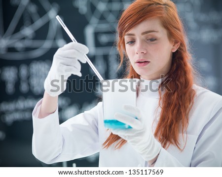 close-up of student in chemistry lab conducting an experiment with colorful liquids and magical gas around a lab table and looking in the camera  with a blackboard on the background