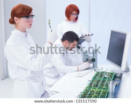 students in a chemistry lab  analyzing a plant and observing chemical reactions under the supervision of a teacher who analyzes under microscope on a lab table with seedlings and lab tools