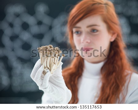 macro of a bunch of mushrooms holded in hands by a preety face student in a chemisty lab with a blackboard on the background