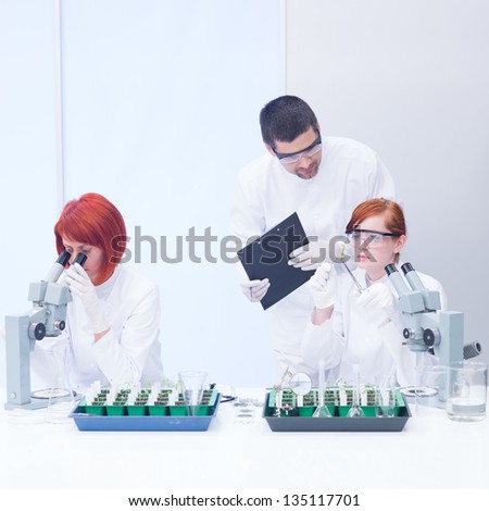 close-up  of a teacher in a chemistry lab supervising the activity on two students analyzing plants on a lab table and  observing reactions under microscope