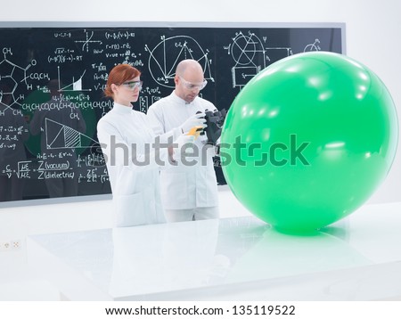 general-view of teacher and student in a chemistry lab scanning a green balloon and a blackboard on the background