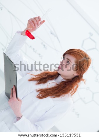 side-view of a beautiful girl student in a chemistry lab analyzing colorful substances and taking notes and white board on the background