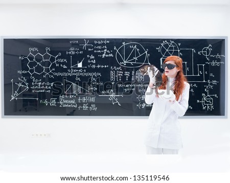 general-view of a pretty girl student in a chemistry lab wearing black glasses and holding a lab pot while analyzing a cat and a blackboard on the background