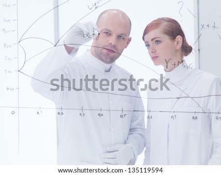 general-view  of a teacher in a chemistry lab drawing and writing formulas  on a transparent board for his student