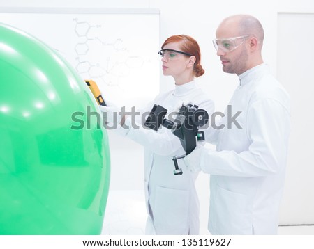 close-up of teacher and student in a chemistry lab scanning a green balloon and a  white board on the background